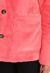 Faux fur jacket in bright pink. Features a patch pocket, round black buttons, and a soft, textured surface. Long sleeves with a relaxed fit.