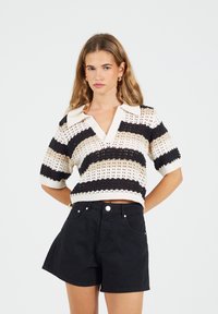 Sweter z dzianiny z krótkim rękawem, z poziomymi paskami w kolorach czarnym, beżowym i białym, z kołnierzykiem w kształcie litery V oraz otwartą teksturą. W zestawie z czarnymi szortami.