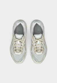 Light grey sports shoes with a textured mesh upper, beige accents, and a padded collar. Features flat laces and a cushioned sole.