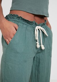 Groene linnen broek met een elastische, gerimpelde tailleband, crèmekleurig trekkoord en zijzakken. Opvallende kenmerken zijn de gestructureerde stof en de casual pasvorm.