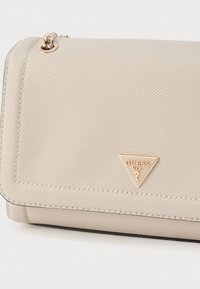 Beige syntetisk håndtaske med tekstureret overflade, trekantet gullogo og syningsdetaljer. Har lukning med klap og kæderem.