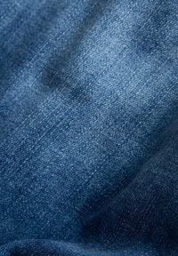 Gros plan sur un tissu en denim bleu montrant une texture tissée détaillée et un ombrage subtil dû aux plis légers.