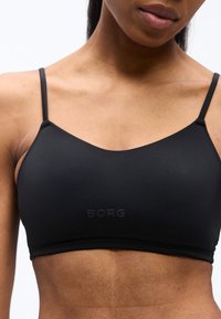 Γυναίκα που φοράει μαύρο αθλητικό σουτιέν με λεπτές τιράντες και το λογότυπο "BORG" στο κέντρο του στήθους, εμφανίζοντας τον άνω κορμό και τον λαιμό.