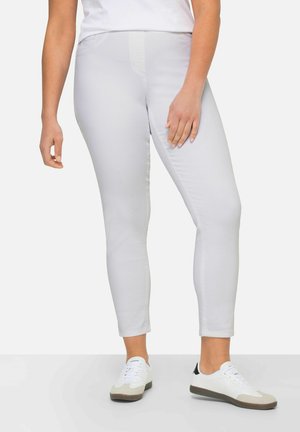 Jeans skinny de color gris claro con una textura suave, que cuentan con bolsillos frontales y una cintura de talle medio, combinados con zapatillas blancas y una camiseta blanca.