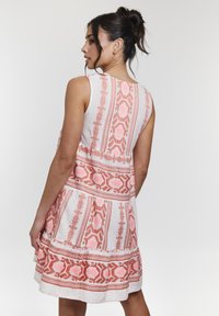 Ärmelloses weißes Kleid mit pinkem, gemustertem gestickten Elementen, ausgestattet mit einem weiten Saum und kontrastierenden Bordüren. Einfaches Design, Leinenstruktur.