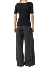 Czarna bluzka z krótkim rękawem i szerokim dekoltem, zestawiona z luźnymi szarymi spodniami. Tkanina wydaje się gładka, o minimalnej fakturze.
