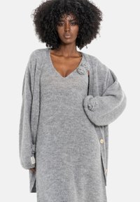Szary oversize kardigan wykonany z miękkiego dzianinowego materiału, z głębokim dekoltem w kształcie litery V i ozdobnymi guzikami z przodu. Teksturowany, przytulny fason.