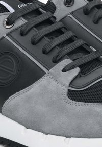 Zwarte en grijze sneakers met suède en synthetisch leer, vlakke zwarte veters, gestructureerde meshpanelen en een witte rubberen zool.