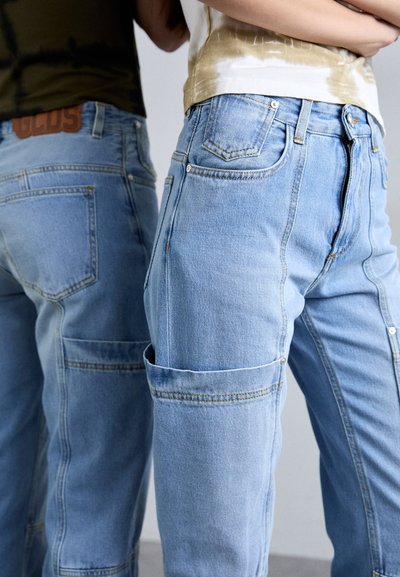 Lys blå denim cargo-bukser med flere lommer, en avslappet passform og kontrastsøm. Har et lærmerke på baksiden.