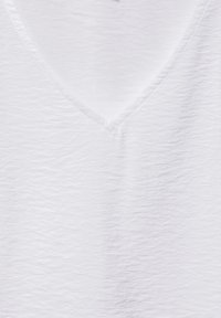 Camiseta blanca de cuello en V texturizada, con una superficie ligeramente arrugada, que muestra un ajuste relajado y un diseño limpio y simple.