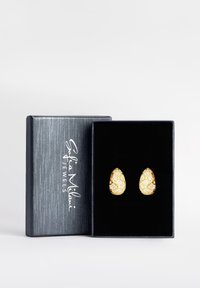 Guld-färgade örhängen i droppform med texturerad yta och diamantliknande detaljer, visade i en svart sammetstrykt låda.