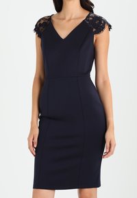 Navy blue fitted dress with a V-neck, cap sleeves made of black lace, smooth fabric, and a knee-length hemline.