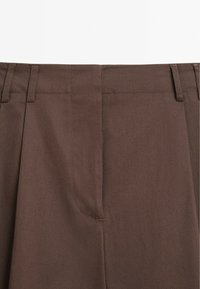 Hnědé kalhoty s hladkým, strukturovaným materiálem. Obsahují plochý střih, záhyby a poutka na pásek. Jednoduchý design zaměřený na funkčnost.