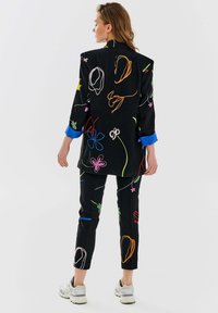 Czarny garnitur z kolorowymi wzorami haftowanymi, z marynarką z podwiniętymi niebieskimi mankietami i dopasowanymi spodniami o slim fit.