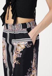 Fekete nadrág virágos paisley mintával, rózsaszín és arany árnyalatokban. Gumis derékrésszel és oldalsó zsebekkel rendelkezik. Sima textúra.