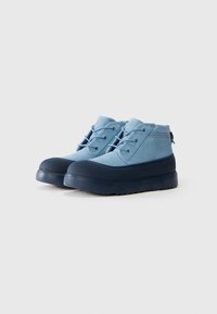 Bottines en daim bleu clair avec semelles en caoutchouc bleu foncé et coques de protection, dotées de trois œillets pour les lacets et de cols rembourrés.