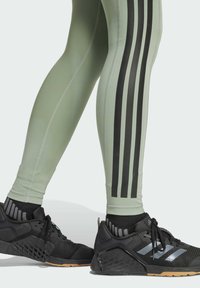 Leggings verde chiaro con strisce verticali nere, abbinati a scarpe da ginnastica nere con un design testurizzato e accenti grigi.