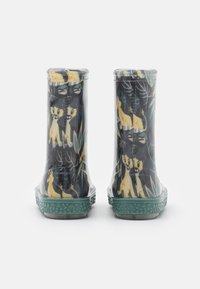 Bottes de pluie pour enfants avec des semelles texturées vertes, présentant un motif imprimé de lionceaux jaunes et de feuillage sur un fond sombre.