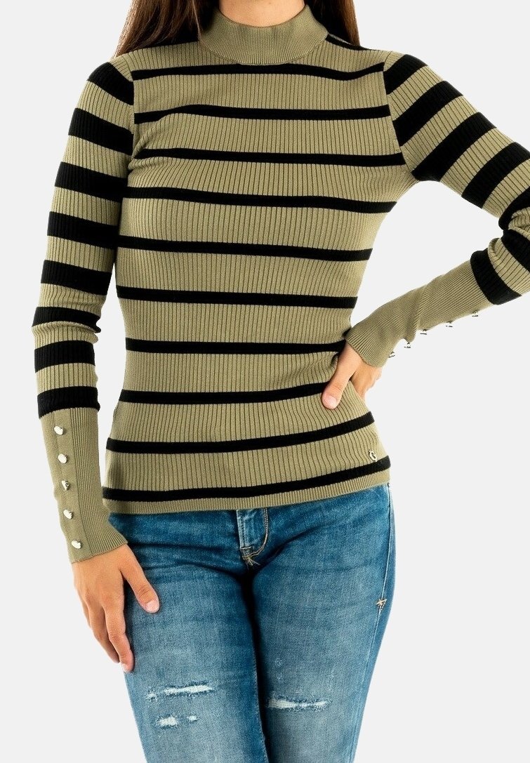 Olijfgroene geribbelde turtleneck met zwarte strepen, voorzien van knoopdetail op de mouwen. Gepaard met versleten blauwe jeans.