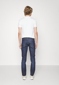 Modré denimové džíny s úzkým střihem a rovnými nohavicemi, s kapsami na zadní straně a rovním pasem. Nosené s bílým tričkem a teniskami.