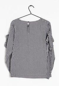 Blouse à carreaux noir et blanc avec des manches longues, des accents froncés, un col rond et une ouverture en forme de clé au dos.