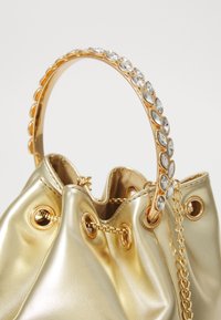 Gouden metallic handtas met een geplooid ontwerp, uitgerust met een kettinghandvat versierd met heldere rhinestones en gouden hardwareaccenten.