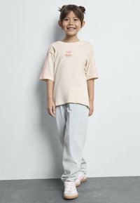 Camiseta beige con logo rosa de Adidas y mangas a rayas, combinada con pantalones holgados de color azul claro y zapatillas con acentos rosas.