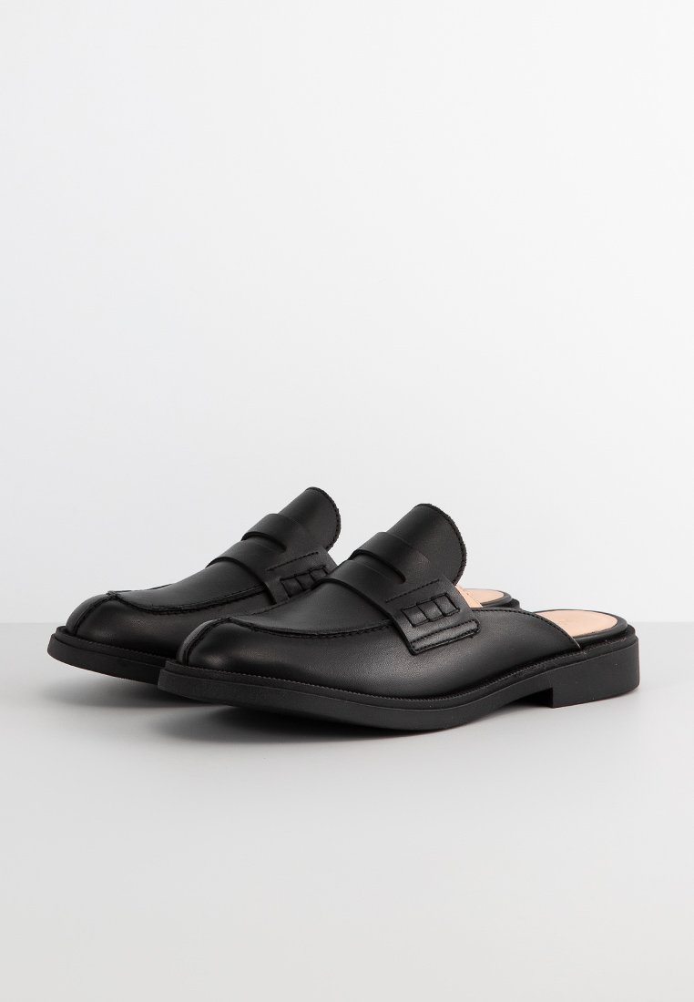 Schwarze Leder-Deckschuhe mit runder Zehenpartie, ausgestattet mit einem Riemen und dekorativen Nähten, flacher Sohle und glatter Oberfläche.