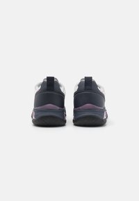 Ett par svarta och vita sportskor med lila detaljer sedd från baksidan, som visar sula textur och hälpullflikar.