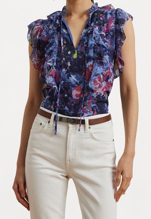 Ærmeløs bluse med flæser i blå, lilla og rød blomsterprint, kombineret med hvide jeans med høj talje og brun bælte.