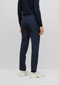 Pantaloni tailored blu marina con una texture liscia, dotati di tasche posteriori e passanti per cintura, abbinati a sneakers bianche.