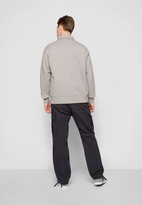Sudadera gris claro con un cuello alto, combinada con pantalones cargo negros que cuentan con bolsillos laterales. La tela parece suave y con textura.