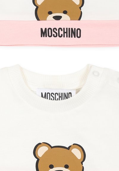 Camicia in cotone bianca con grafica di un orso bruno, caratterizzata da un colletto a righe rosa con la scritta "Moschino" stampata in nero. Dettaglio dei bottoni sulla spalla.
