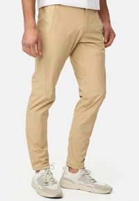 Pantalons beige ajustés en tissu léger et lisse. Équipés de poches latérales et d'une coupe droite. Portés avec des baskets de couleur neutre.