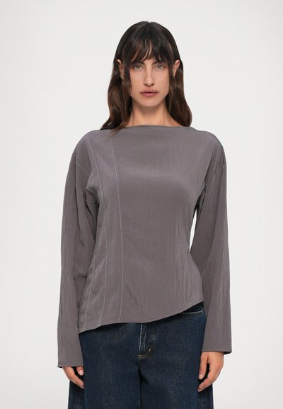 Gray long-sleeve top with a boat neckline, featuring side seam detailing and a slightly curved hem, paired with dark denim jeans.