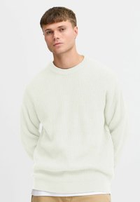 Lys grønn ribbestrikket genser med rund hals og droppede skuldre, laget av et teksturert strikket stoff. Modellen har på seg beige bukser.
