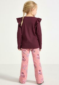 Tummanpunainen pitkähihaisen paita, jossa röyhelöt olkapäillä, yhdistetty vaaleanpunaisiin liehulahkeisiin housuihin, joissa on kukkakuviot eri sävyissä.