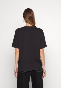 Černé bavlněné tričko s uvolněným střihem, krátkými rukávy a kulatým výstřihem. Zadní strana je bez grafiky a má jednoduchý design.