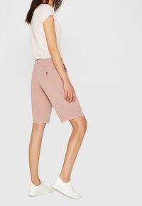 Shorts in denim rosa chiaro con taglio dritto, tasche laterali e dettagli di cucitura sottili, abbinati a una maglietta bianca a maniche corte e sneakers bianche.