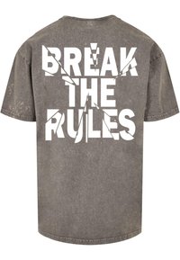 Grijze, oversized katoenen t-shirt met gedurfde witte letters die zeggen "BREK DE REGELS" met een versleten textuur en een ontspannen pasvorm.