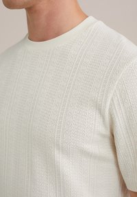 Mezgimas suapvalinta kaklo linija šviesiai baltos spalvos, su tekstūruotu raštu ir subtiliomis vertikaliomis juostelėmis bei minkšta, kvėpuojančia medžiaga.