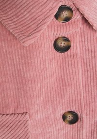 Tessuto di velluto a coste rosa con righe verticali, caratterizzato da due grandi bottoni scuri e un colletto a punta, che mette in mostra una superficie texturizzata.