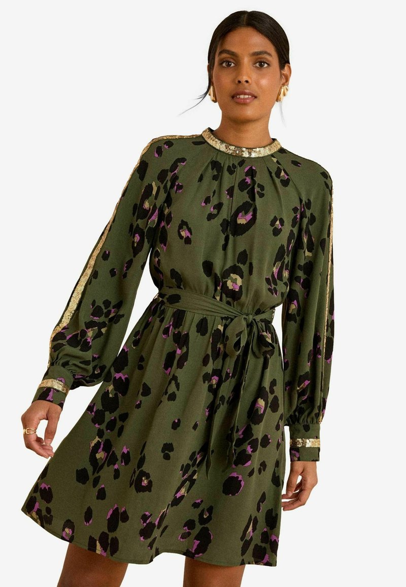 Rochie verde cu imprimeu leopard negru și mov. Dispune de mâneci lungi, guler plisat, accente aurii pe manșete și o talie legată.