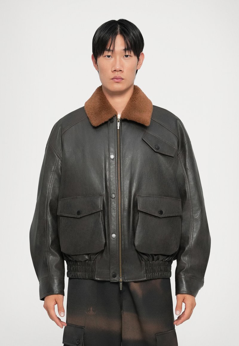 Black leather bomber jacket with a brown faux fur collar, featuring two front pockets, elasticated waistband, and a front zipper closure.