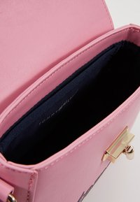 Rosa læderhåndtaske med en glat overflade, indeni beklædt med mørkeblå stof, med guldfarvet hardware og klaplukning.