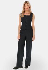 Czarny garnitur w paski, składający się z topu bez rękawów z kwadratowym dekoltem i guzikami oraz spodni o szerokich nogawkach, wykonany z teksturowanej tkaniny.