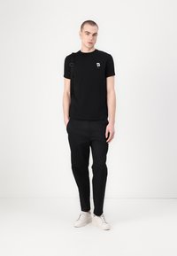 Černé tričko s krátkým rukávem a malou bílou grafikou na hrudi, doplněné černými kalhotami a bílými teniskami. Jednoduchý, sportovní design.