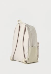 Ανοιχτό μπεζ σακίδιο πλάτης με δύο επενδυμένους ιμάντες, ένα επάνω χερούλι και μια πλάγια τσέπη σε αντίθετη απόχρωση. Κατασκευασμένο από ανθεκτικό ύφασμα.