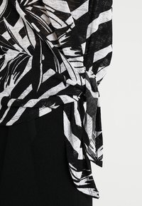 Czarna i biała wzorzysta bluzka z luźnym krojem, teksturowaną tkaniną i wiązaniem po boku. Projekt zawiera abstrakcyjne kształty liści.