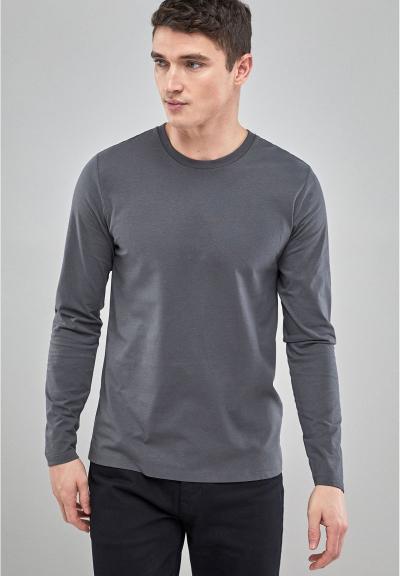 Hallisest long-sleeve T-särk sileda kangaga, ümmarguse kaelusega, sobiva disainiga ja minimalistlikus stiilis, koos mustade pükstega.